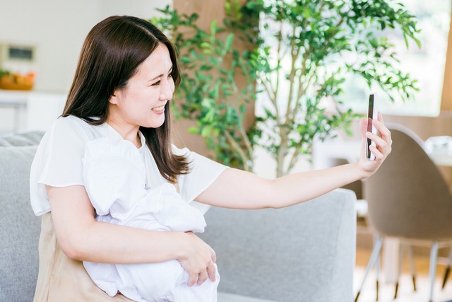 スマートフォンで赤ちゃんと写真を撮る女性