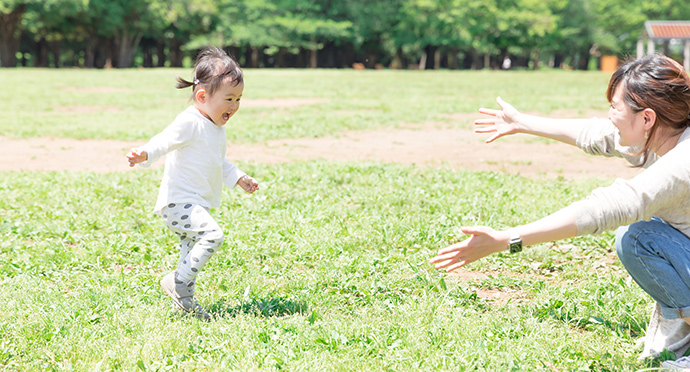 走る子供を笑顔で迎える女性保育士の様子を写した画像