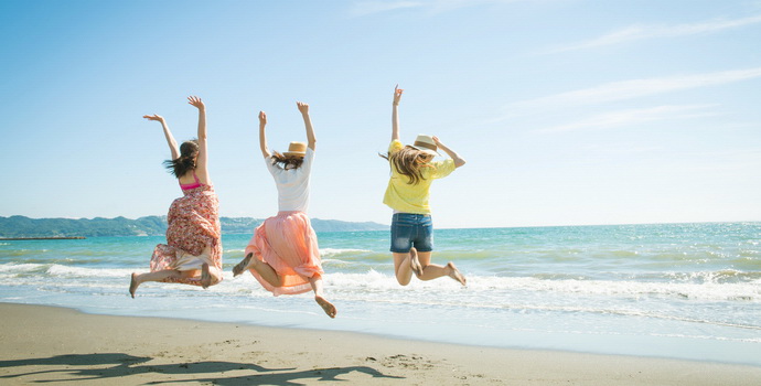 海に向かって砂浜でジャンプする女性３人組を写した写真